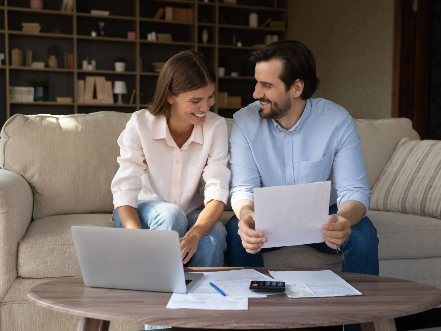 Couple sitting on a couch reviewing bills and budgeting on a laptop, planning their next move during tax refund season.