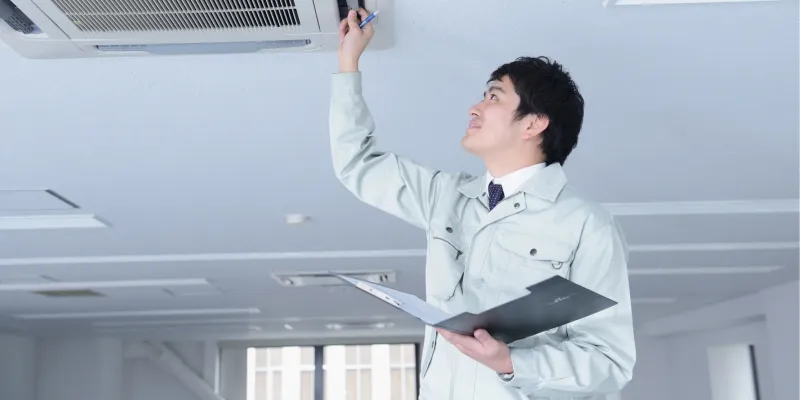 Technician inspecting a ceiling HVAC unit during preventative property maintenance in Hernando, MS